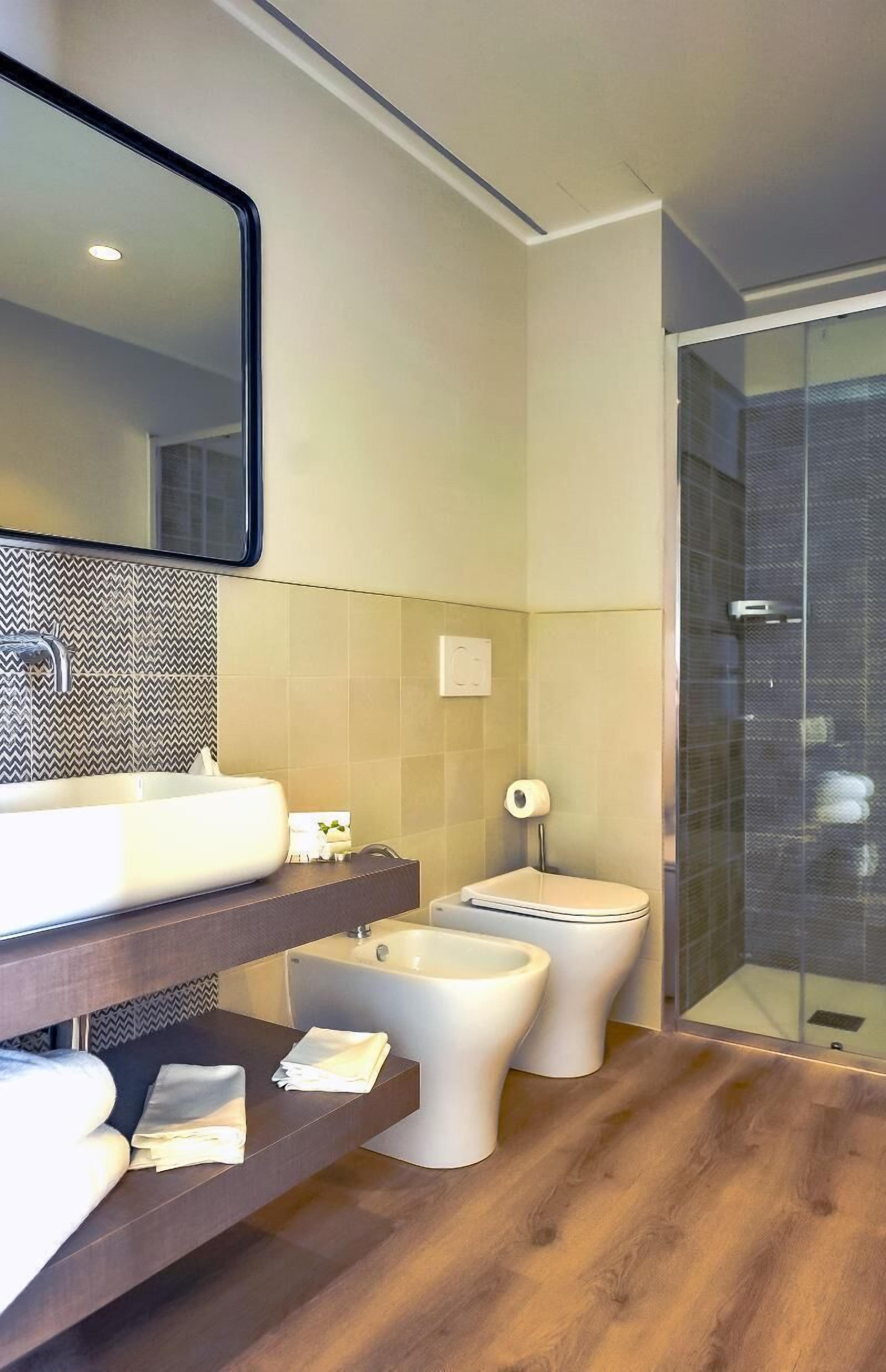 A modern bathroom with a large mirror, a sink, two toilets, and a shower area.