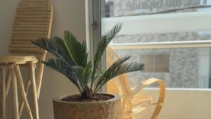Una planta en maceta sobre un soporte con ruedas cerca de una ventana que ofrece vistas a edificios.