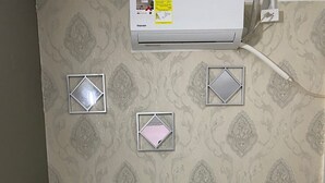 A neatly made bed with white linens, a dark wooden headboard, and a wall-mounted air conditioner.