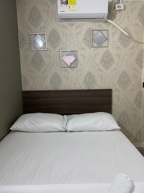 A neatly made bed with white linens, a dark wooden headboard, and a wall-mounted air conditioner.
