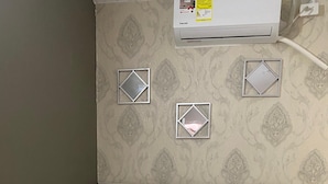 Una cama bien tendida con ropa blanca y una almohada gris estampada, un cabecero de madera y un equipo de aire acondicionado instalado en la pared.