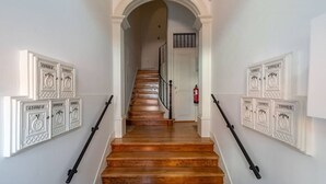 Un escalier avec des marches en bois et des rampes noires, de part et d’autre duquel se trouvent des boîtes aux lettres blanches ornées de motifs en relief.