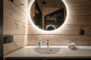 Une salle de bain rustique, avec des murs en bois, un miroir rond, un lavabo et une serviette.