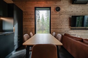 Une cuisine moderne avec une table et des chaises en bois, un four encastré et une grande fenêtre donnant sur la forêt.