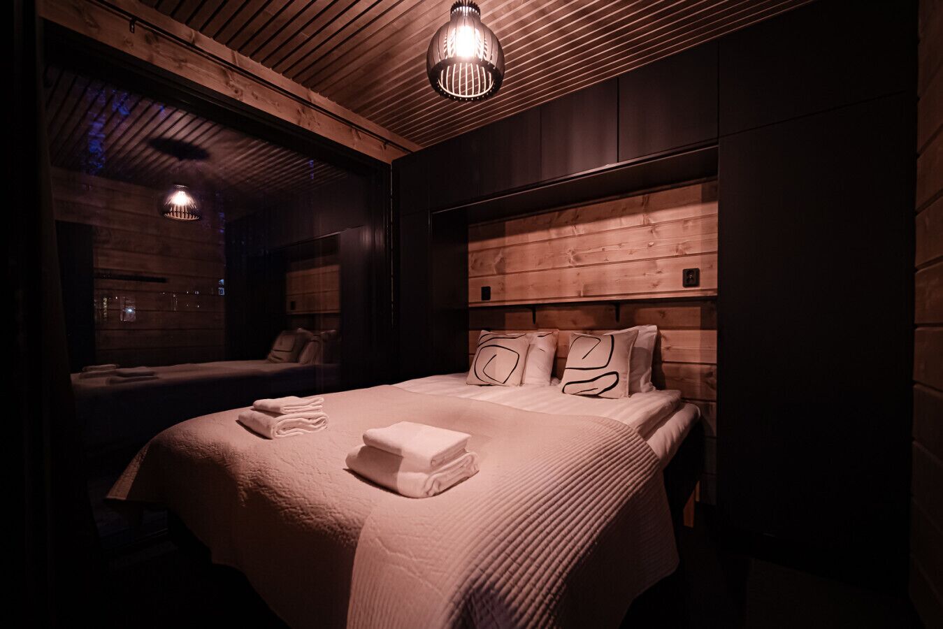 Una habitación de hotel moderna con cabecera de madera, una cama grande con toallas ordenadas y un ventanal con vistas al exterior.