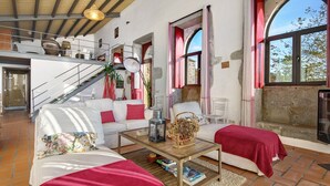 Amplia sala de estar con una escalera, sofás blancos, una mesa de centro de madera y ventanas grandes.