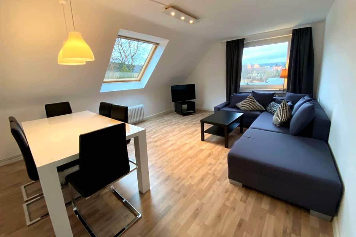 Ein modernes Wohnzimmer mit Essbereich, einer Sofagarnitur, einem Fernseher und einem Oberlicht.