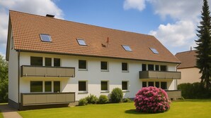 A two-story residential building with a tiled roof, multiple balconies, and a well-maintained lawn with a large flowering shrub. - Tanne 16 (Braunlage)