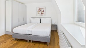 A modern bedroom with a bed, a wardrobe, a small bedside table, and a window with a view. - Castle apartment in the center of Rapperswil - Schnydershome (Rapperswil-Jona)
