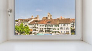 A window with a view of a town featuring traditional European architecture, including buildings with gabled roofs and a prominent tower. - Castle apartment in the center of Rapperswil - Schnydershome (Rapperswil-Jona)