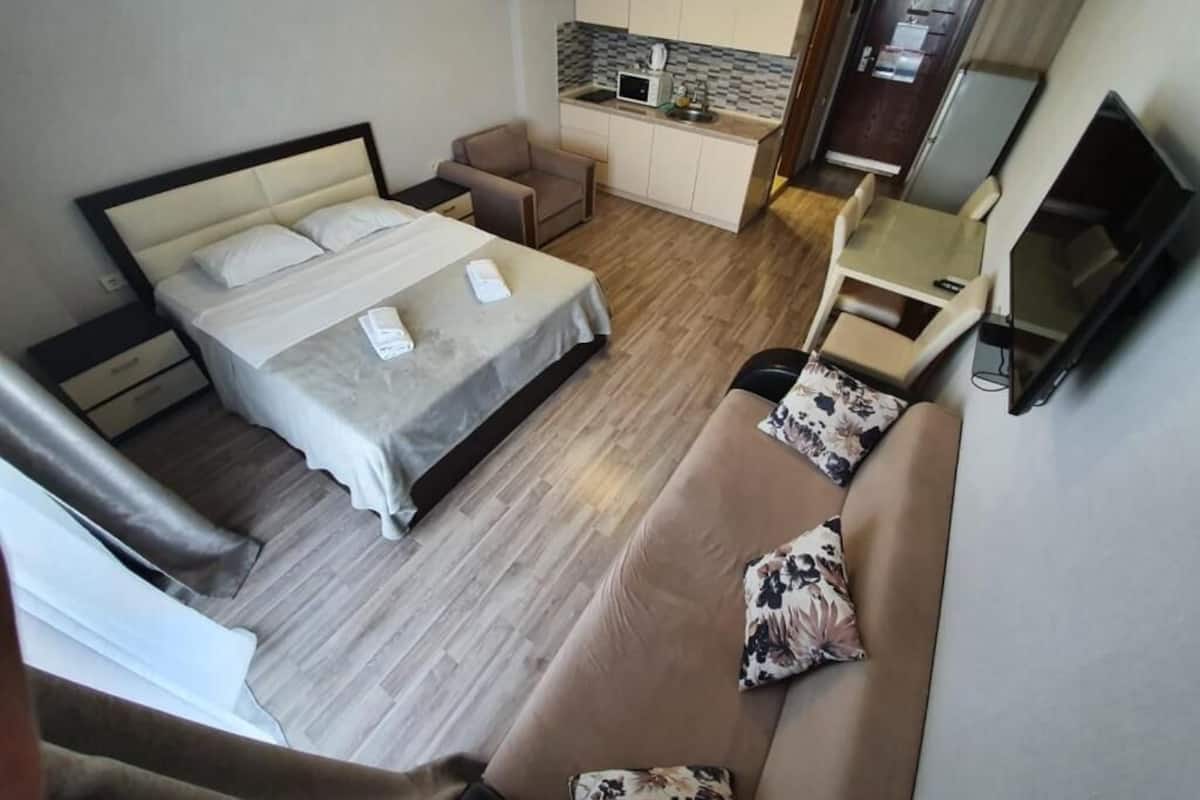 A compact hotel room with a bed, a sofa, a small kitchenette, and a TV.