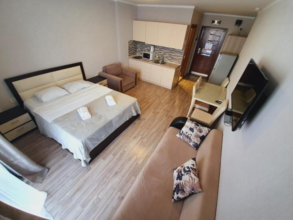 Kompakti hotellihuone, jossa on sänky, sohva, pieni keittopiste ja televisio.