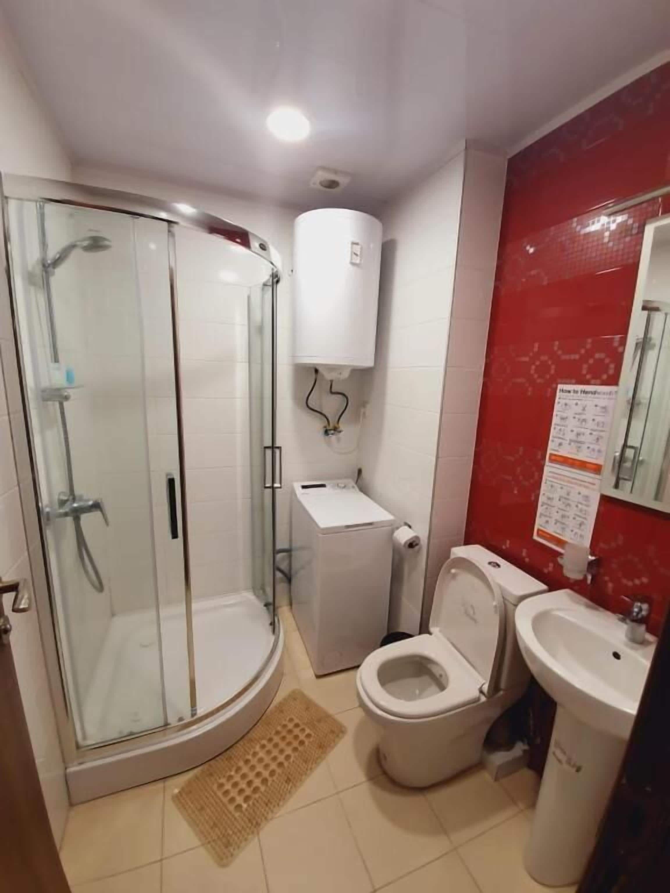 A bathroom with a glass-enclosed shower, a toilet, a sink, and a white washing machine.