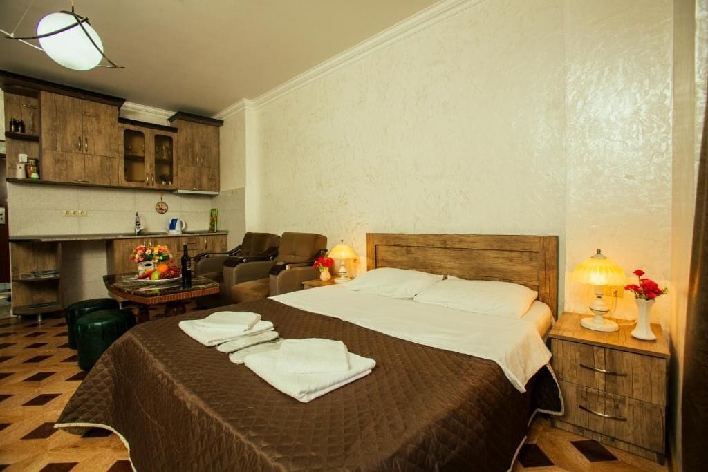 Une chambre d’hôtel avec un grand lit, une tête de lit en bois, un bureau avec une chaise et une petite table avec une lampe et des fleurs.