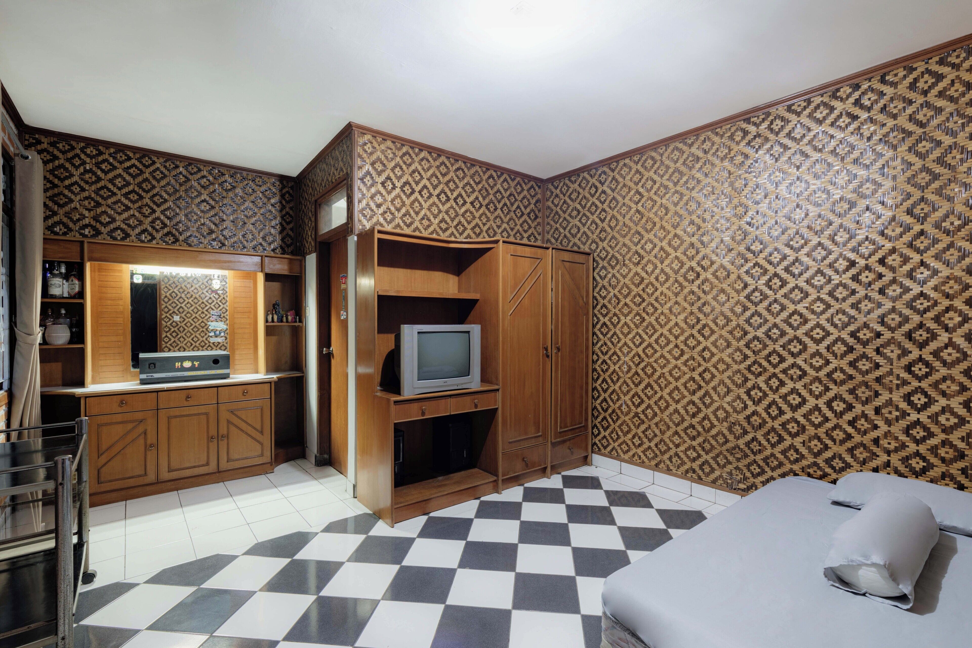 A compact hotel room with a checkered floor, wooden furniture, a television, and patterned wallpaper.