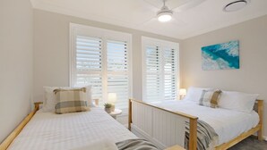 A bedroom with two single beds, white walls, a ceiling fan, and a window with blinds. - Coastal Drift – your Jervis Bay escape starts here (Callala Bay)