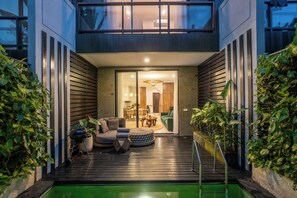 En moderne udendørs terrasse med pool, siddeområde og udsigt til huset.