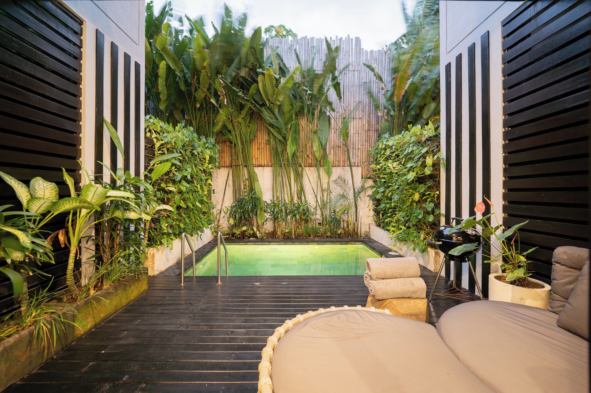 A pool area with a wooden deck, lounge chairs, and tropical plants.