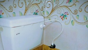 A toilet with a white tank and seat, connected to a wall-mounted pipe. - THE ROYAL STAY IN (Hyderabad)