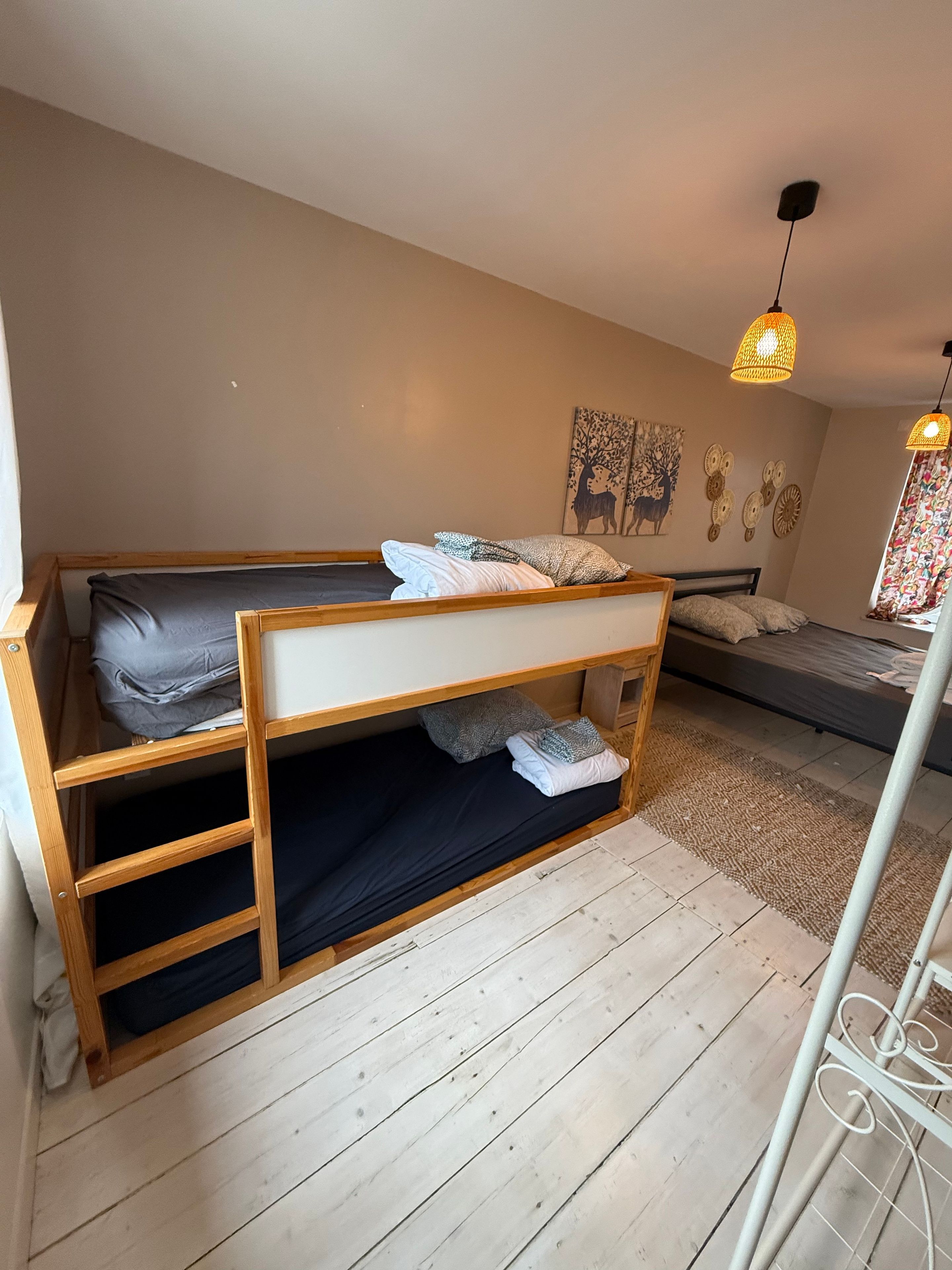 Dormitorio con literas, una escalera de madera, una mesita y una ventana con cortinas.