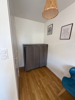 A room with a wooden floor, a grey curtain, a blue chair, and a hanging light fixture.