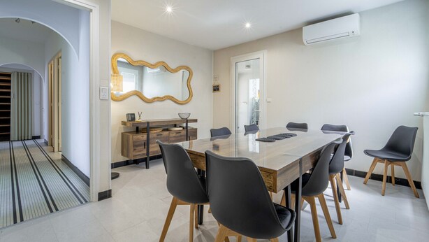 Un comedor moderno con una mesa rectangular grande, seis sillas, un aparador de madera y un espejo grande en la pared.