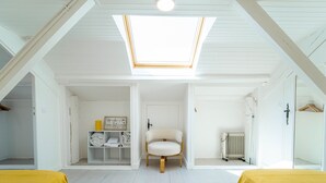 Una habitación con tragaluz, dos camas con ropa de cama amarilla, una silla, un radiador y un estante con ropa doblada.