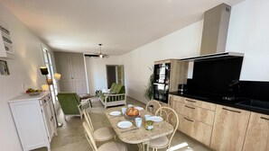 Una cuina moderna amb zona de menjador, armaris blancs i taulell negre.