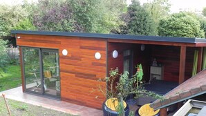 A modern house with a wooden exterior, large sliding glass doors, and a patio area with outdoor seating.