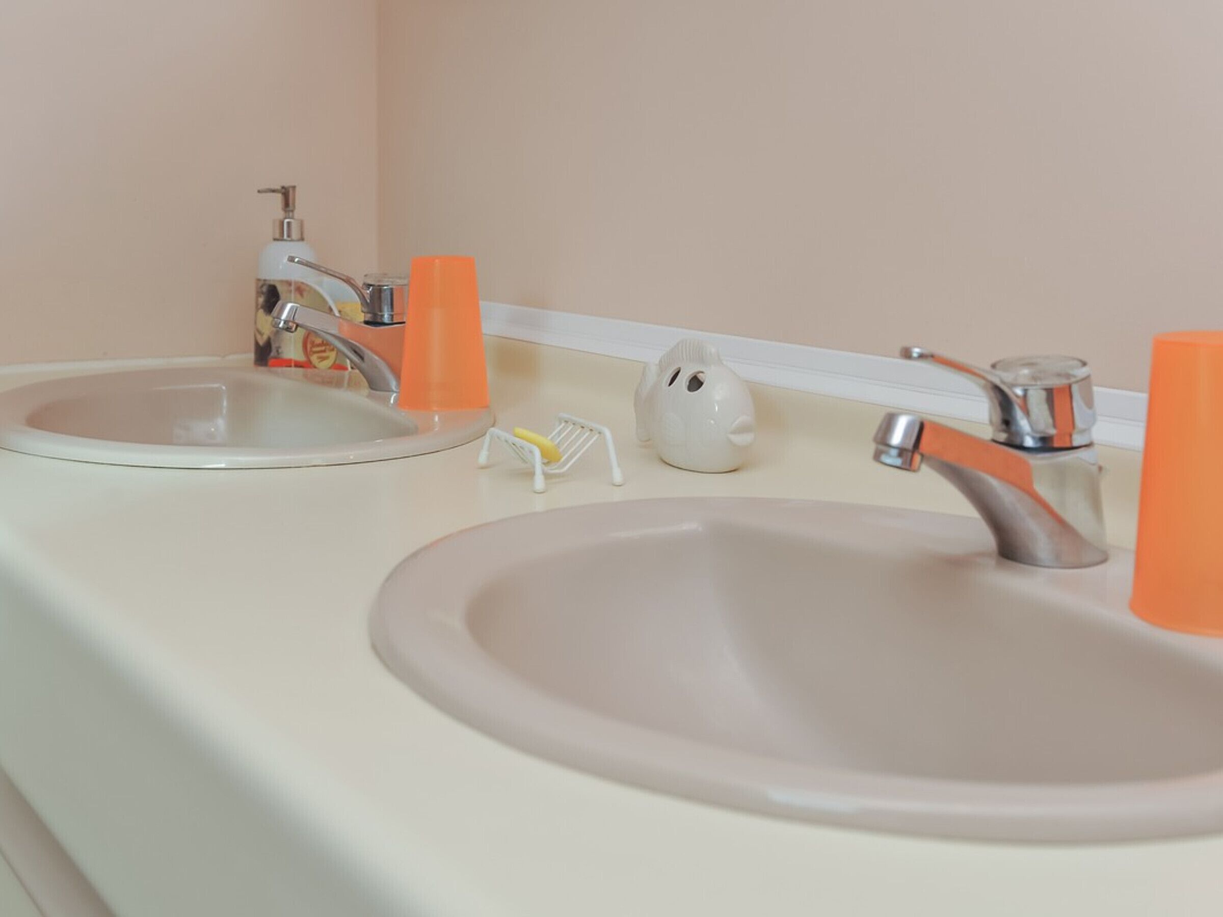 A bathroom with two sinks, a mirror, and orange soap dispensers.