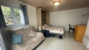 A compact room with a sofa, a bed, a small desk, and a window with curtains.