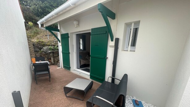 A covered outdoor seating area with a table and chairs, a small table, and a barbecue grill.