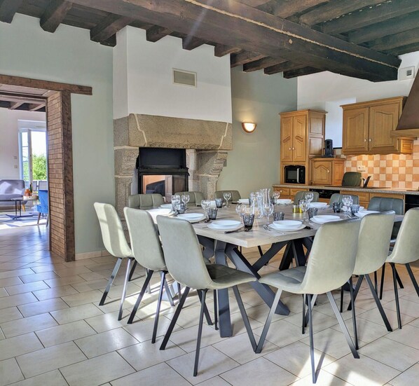 A dining area with a stone fireplace, a kitchen with wooden cabinets, and a view of the outdoors. - Chez Juliette: Family Cottage with Games Room and Fireplace (Chantrigné)
