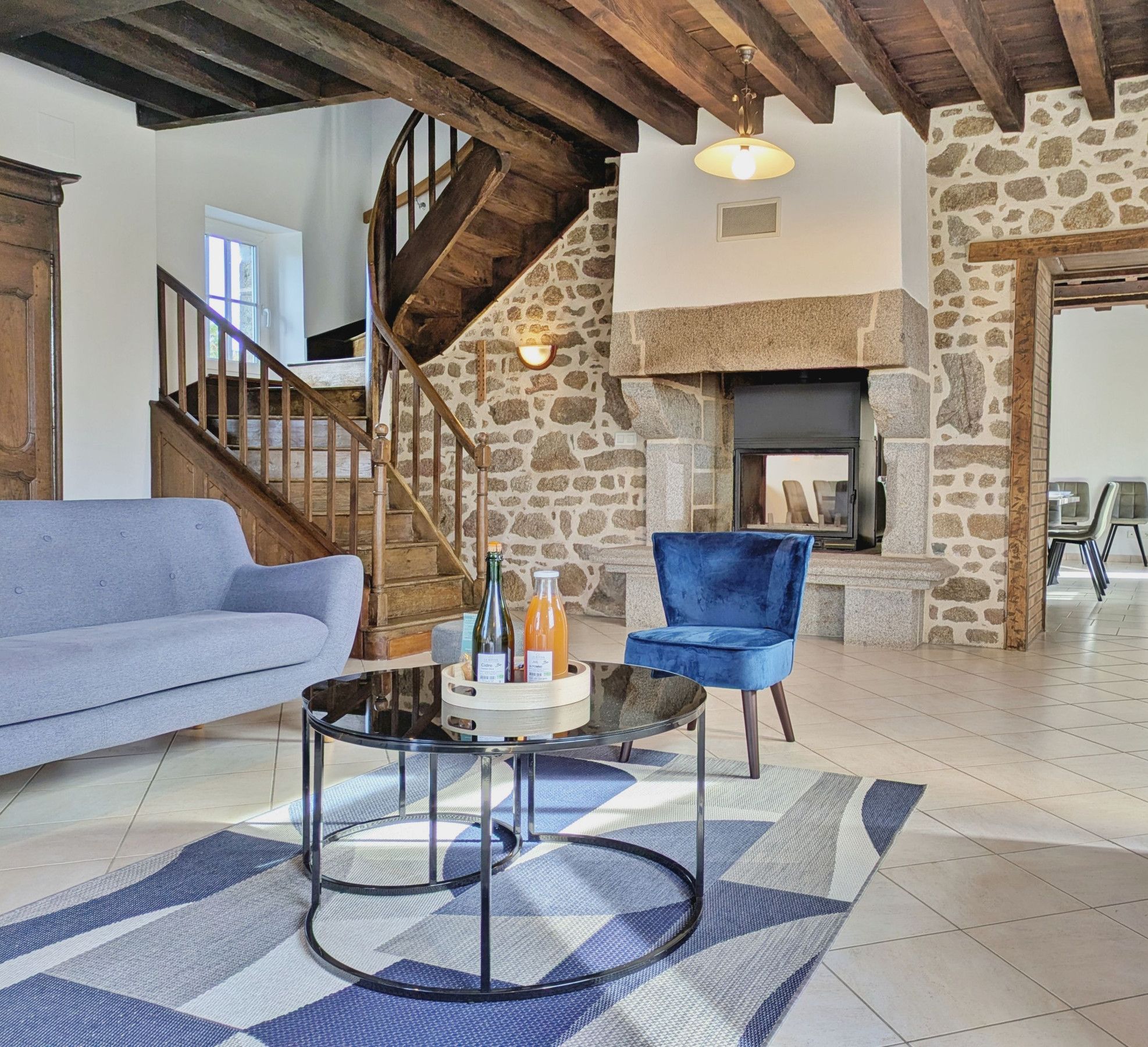 Ein geräumiger Wohnbereich mit Kamin aus Stein, blauem Sessel, Sofa und einer Treppe, die zu einer weiteren Ebene führt.