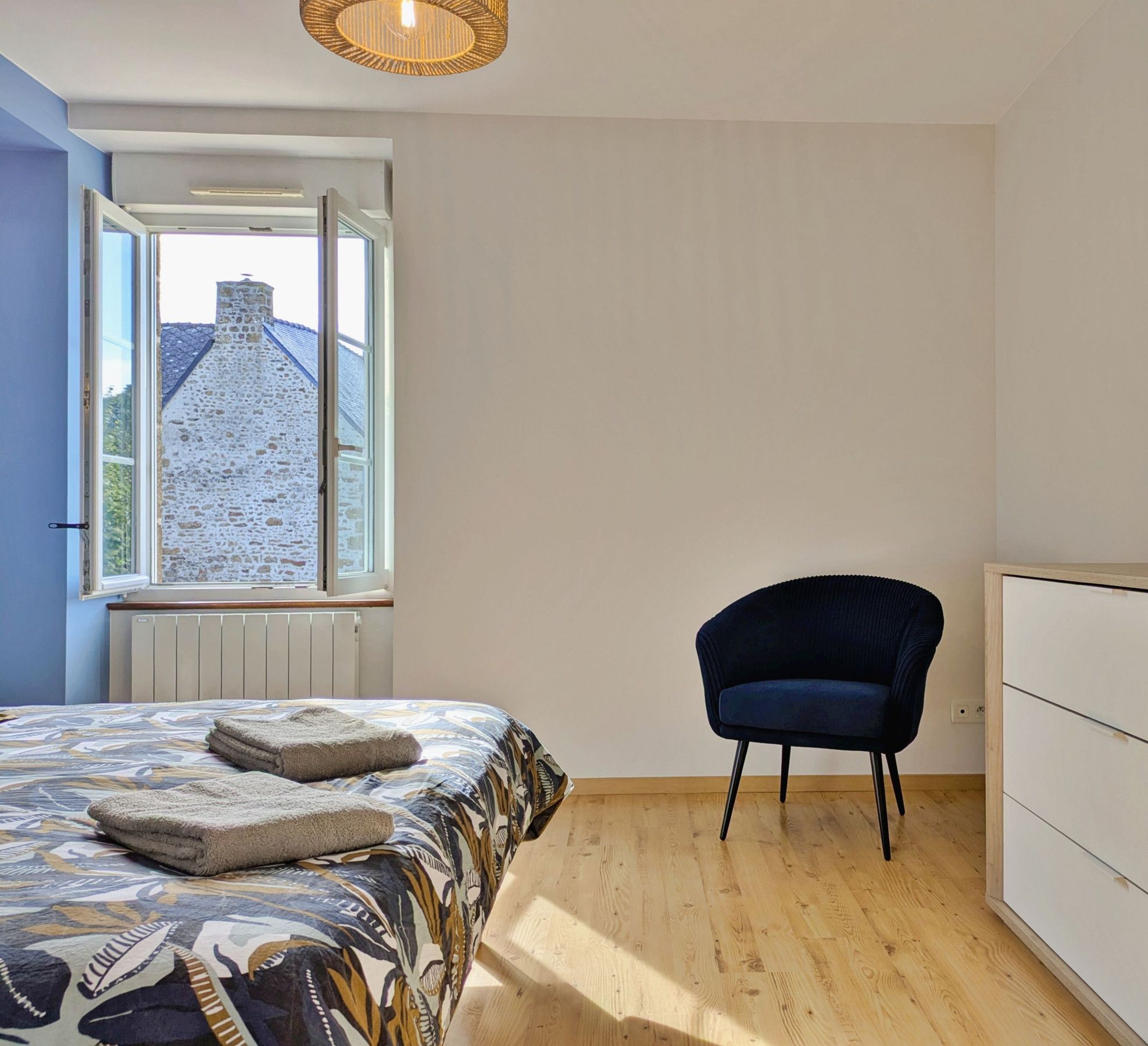 A bedroom with a bed, a chair, a dresser, and a window with a view of a building.