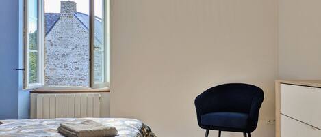 A bedroom with a bed, a chair, a dresser, and a window with a view of a building.