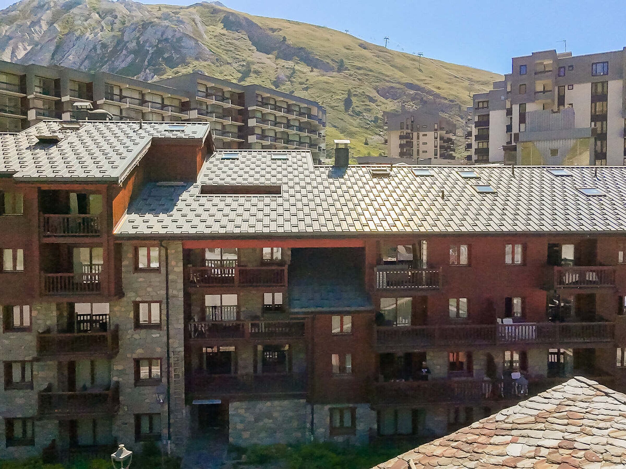 A multi-story building with balconies, a mountain in the background, and a clear sky.