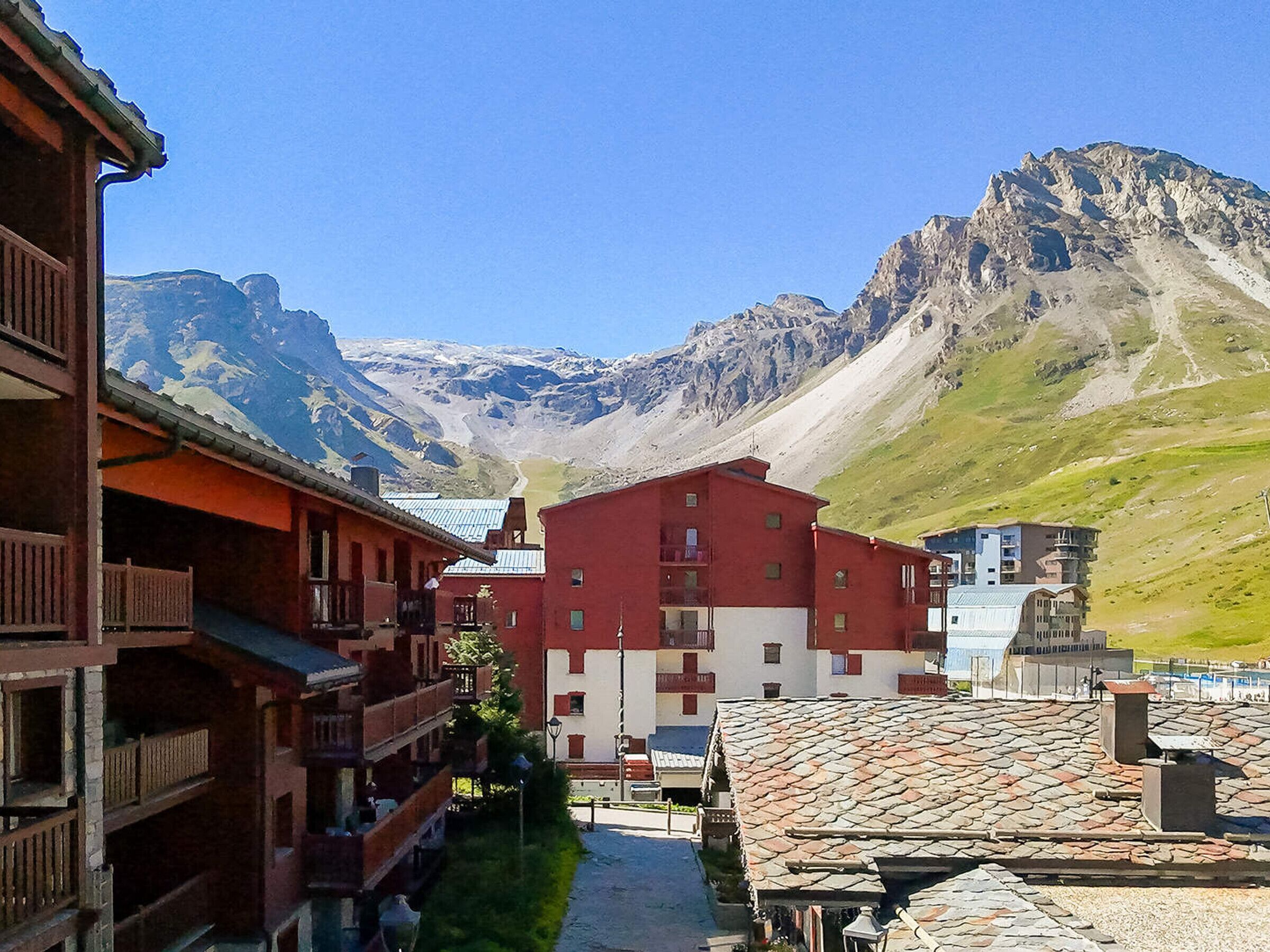 A traditional chalet-style building with a red facade and a stone roof, set against a backdrop of mountains and clear skies.