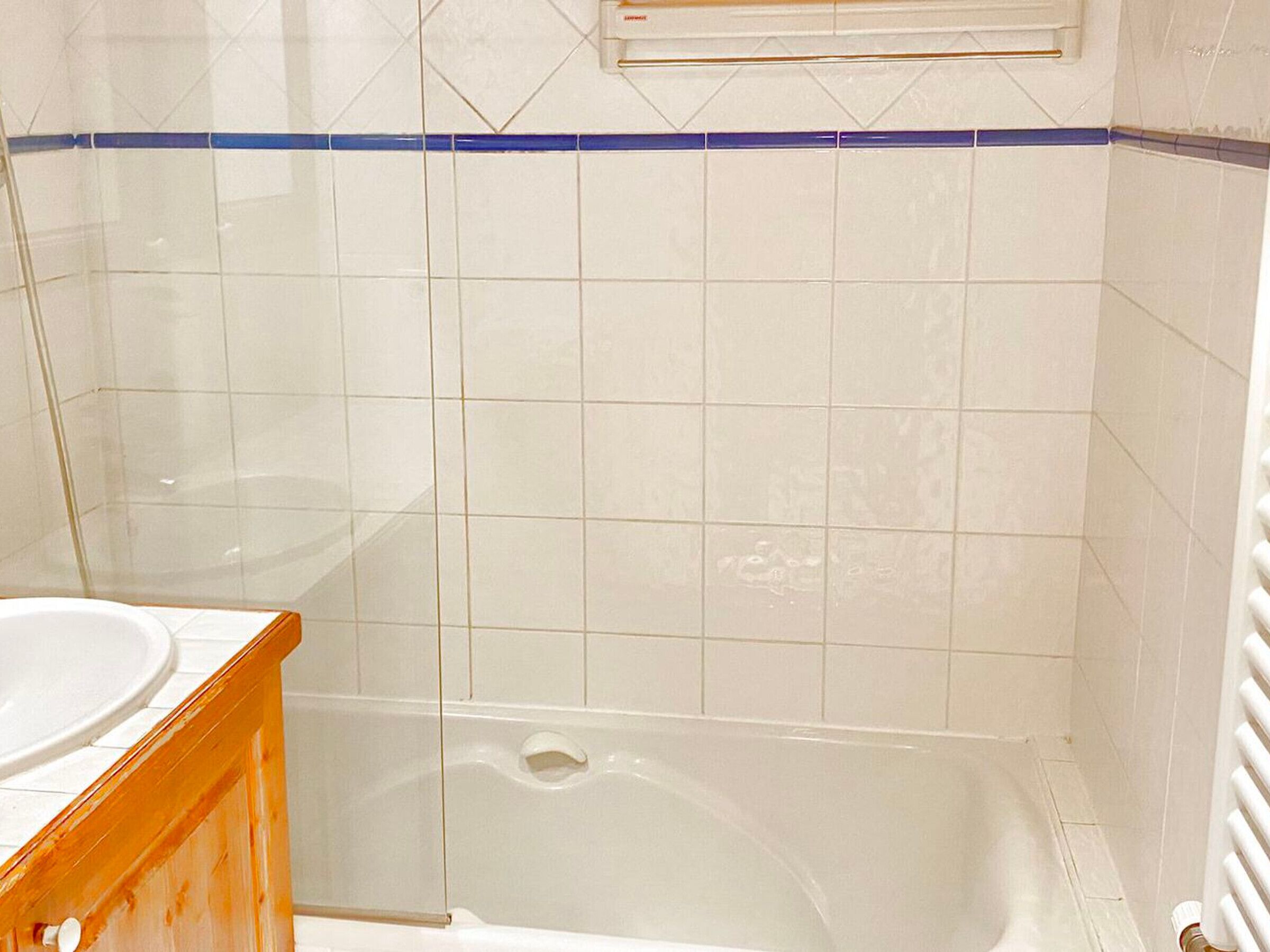 Ein Badezimmer mit weißen Fliesen, einer Badewanne und einer Duschkabine aus Glas.