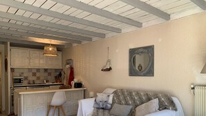 A cozy living room with a sofa, a coffee table, and a small stool. There is a kitchen area with cabinets and a hanging light fixture. - Spacious Studio in Pra-Loup 1600 | 4 pers, balcony, WIFI (Pra-Loup)