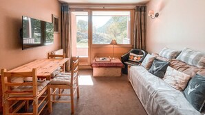 Ein gemütliches Zimmer mit Holztisch, Stühlen, einer Couch und einem an der Wand befestigten Fernseher.