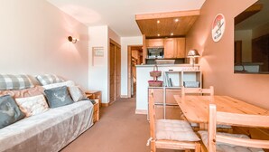 Ein gemütliches Wohnzimmer mit einer Couch und einem Esstisch mit Stühlen. Es gibt eine Küchenzeile mit Holzschränken und einem Spülbecken.