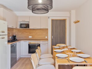 A compact kitchen with white cabinets, a microwave, a coffee maker, and a dishwasher. There is a wooden dining table set with plates, glasses, and cutlery. - Family apartment 4 adults + 4 children, near village, parking (Le Monêtier-les-Bains)
