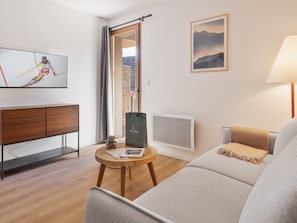 Una sala de estar moderna con un sofá, una mesa de centro, un televisor, un cuadro enmarcado y una ventana con vistas a un edificio.