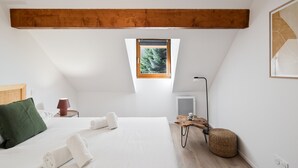 A bedroom with a sloped ceiling, a skylight, a bed with white linens, a green pillow, a wooden nightstand, a lamp, and a woven pouf. - Family apartment 4 adults + 4 children, near village, parking (Le Monêtier-les-Bains)