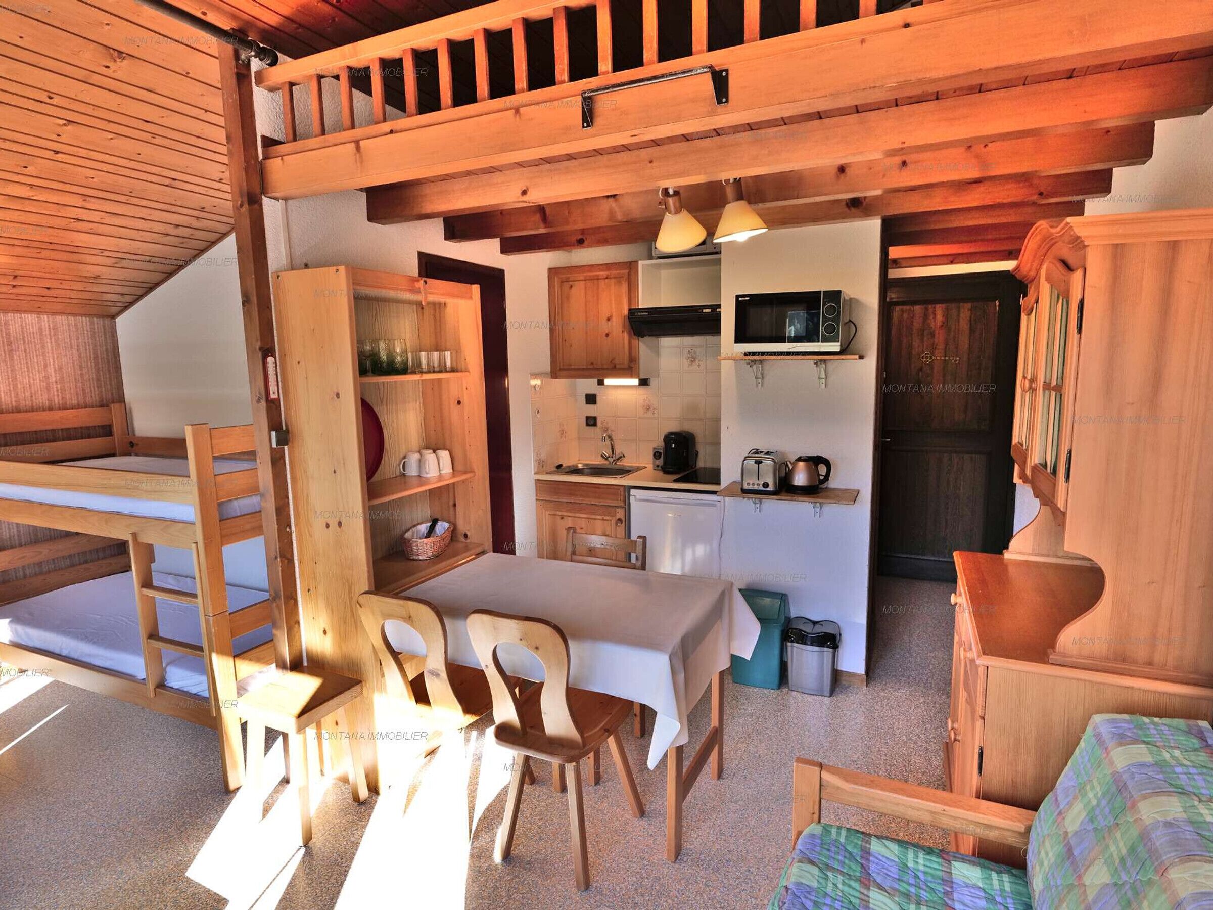 A compact kitchen with wooden cabinets, a microwave, and a sink. There is a dining area with a table and chairs.