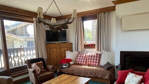A cozy living room with a wooden coffee table, a sofa with plaid cushions, a leather armchair, and a television on a wooden cabinet.