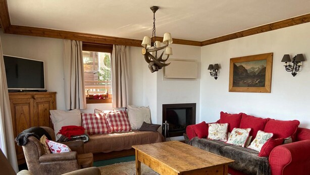 A cozy living room with a fireplace, a wooden coffee table, and two sofas with red cushions.