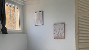 A bedroom with a bed, a window with curtains, a hanging light fixture, and two framed pictures on the wall. - Studio in the heart of the village (Hauterives)