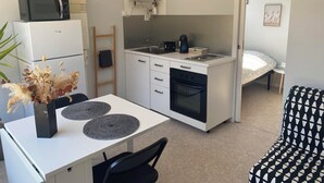 A compact kitchen with a microwave, stove, and sink. There's a small dining table with a vase of dried flowers. A bed is visible in the background. - Studio in the heart of the village (Hauterives)